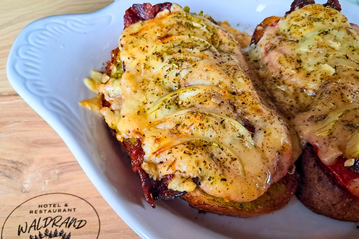 Plat savoureux cuit au four et recouvert de fromage fondu, élégamment servi sur une planche en bois avec le logo de l'Hôtel Restaurant Waldrand.